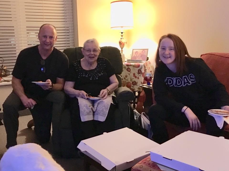 Family sitting together on a couch. Including a Mother, Son and Granddaughter. They are supporting Grandma through end of life care as she ages while her granddaughter is have transformative moments leaning about strength and hardship from her grandma